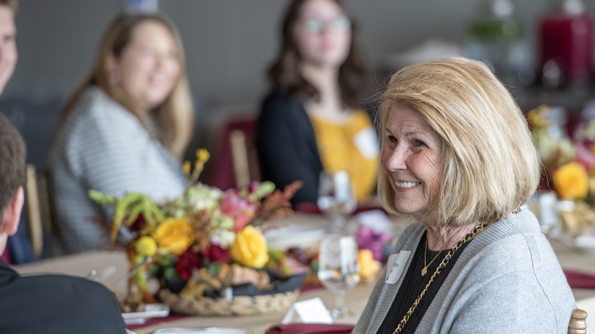 A woman seated at a table smiles off camera